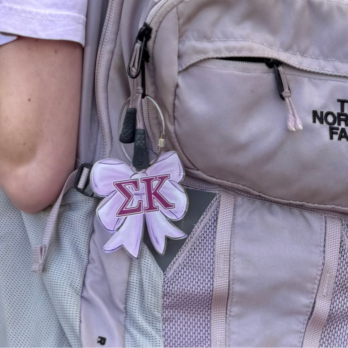Lavender Acrylic Bow Bag Tag attached to book bag for sample