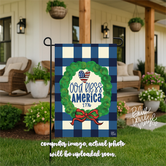 Decorative garden flag with 'God Bless America' design on a checkered background, displayed outdoors.
