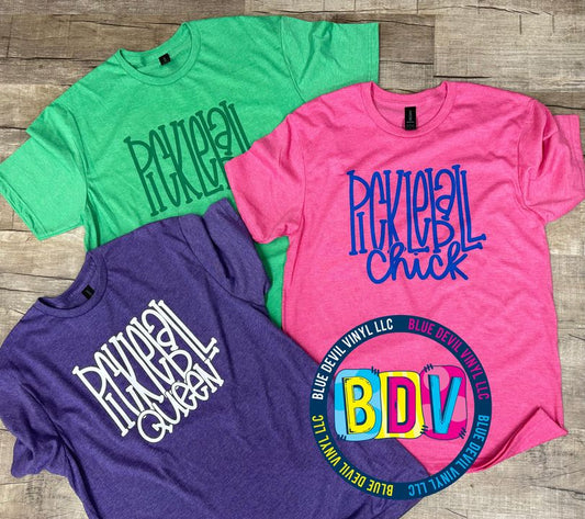 Green T-shirt with Pickleball in green vinyl, Pink T-shirt with Pickleball Chick in Royal Blue Vinyl, Purple T-shirt with Pickleball Queen in White vinyl.