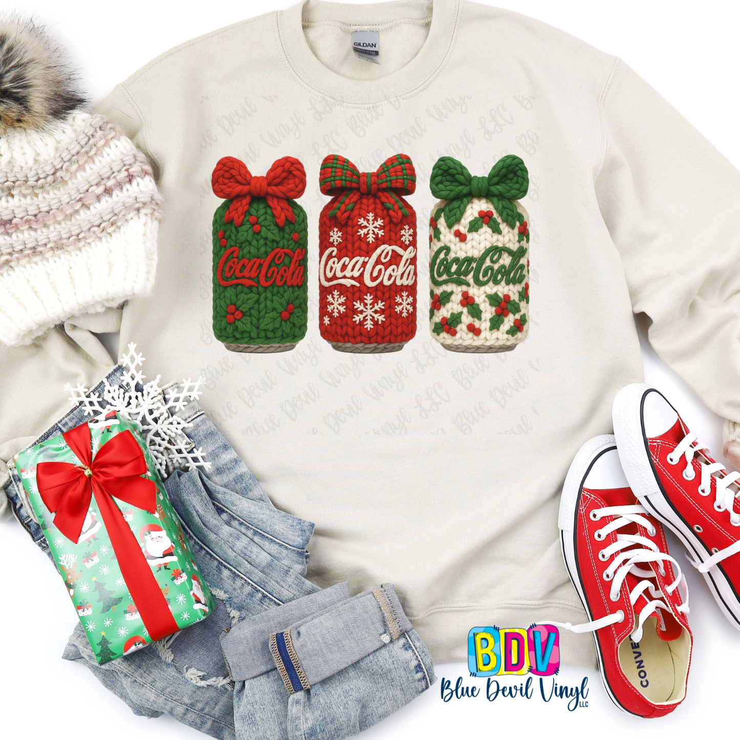 White sweatshirt with Coca-Cola-themed designs, surrounded by festive items like red Converse shoes and a gift bag.